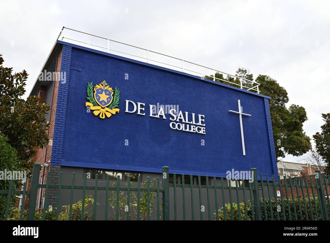 De La Salle College Emblem und Kreuz auf der blauen Außenwand eines Gebäudes am Tiverton Campus der katholischen Schule, hinter einem grünen Zaun Stockfoto