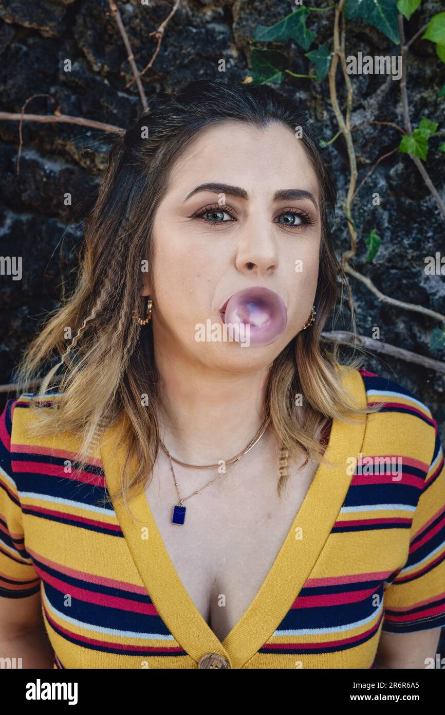 Junge weiße Frau bläst Kaugummi in Ballonform - verspielte und sorgenfreie Momente im Freien Stockfoto