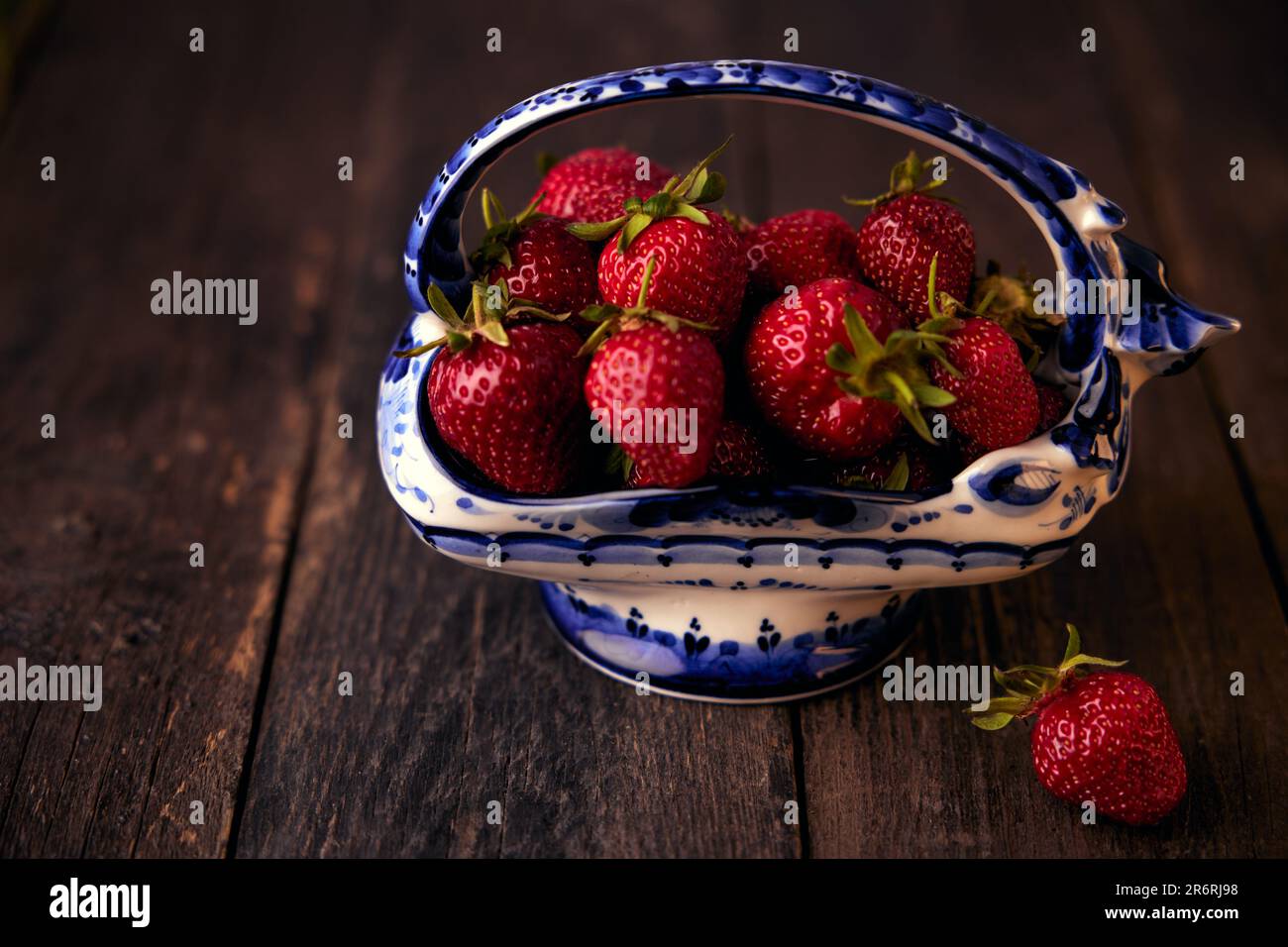 Erdbeeren in einer Porzellanvase mit blauem Ornament auf einem Holztisch. Stockfoto
