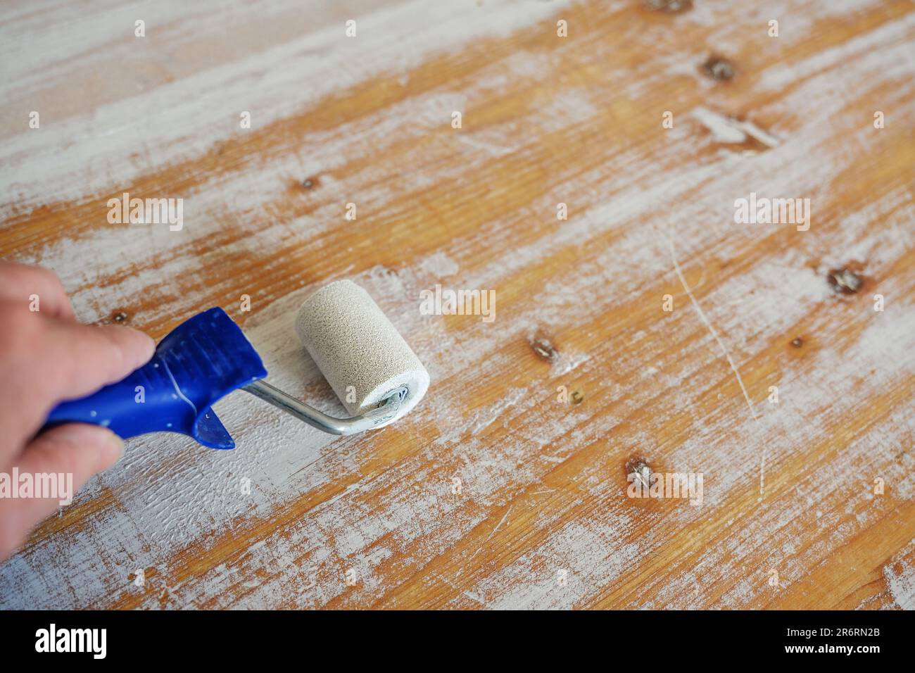 Hand mit Malerwalze erneuert die Glasur auf der Oberfläche eines alten Holztischs, machen Sie es selbst Möbelrenovierung oder Handwerkkonzept, Kopierraum, auswählen Stockfoto