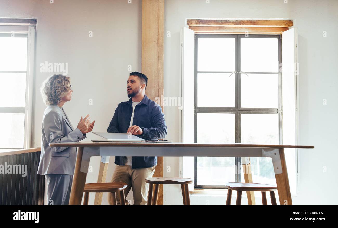 Zwei Geschäftsleute, die in einem Coworking-Bereich eine Diskussion führen. Geschäftskollegen sprechen, während sie zusammen stehen. Geschäftsleute arbeiten zusammen Stockfoto