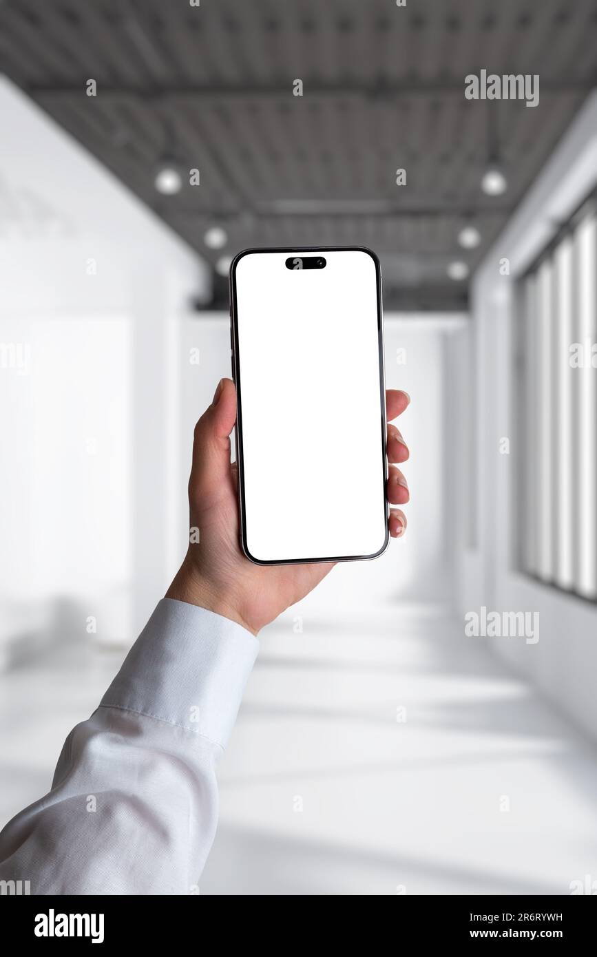 Telefon in Frauenhand mit weißem Hemd. Unternehmenszusammensetzung in einem beleuchteten weißen Büro. Isolierter Bildschirm für App-Präsentation, Modell Stockfoto