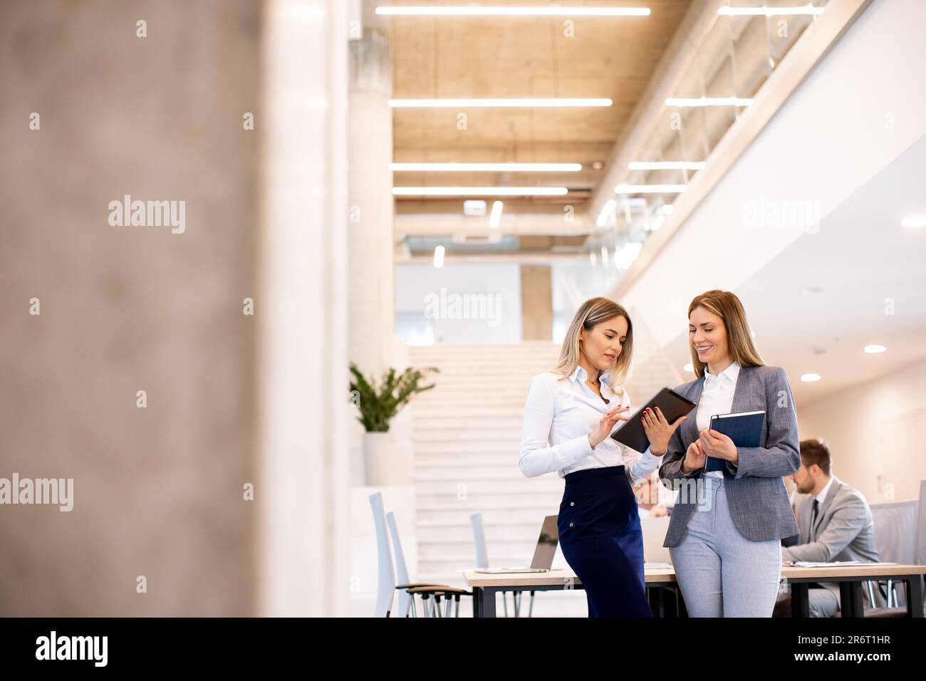 Zwei hübsche junge Geschäftsfrauen, die sich die finanziellen Ergebnisse auf einem digitalen Tablet vor ihrem Team im Büro ansehen Stockfoto