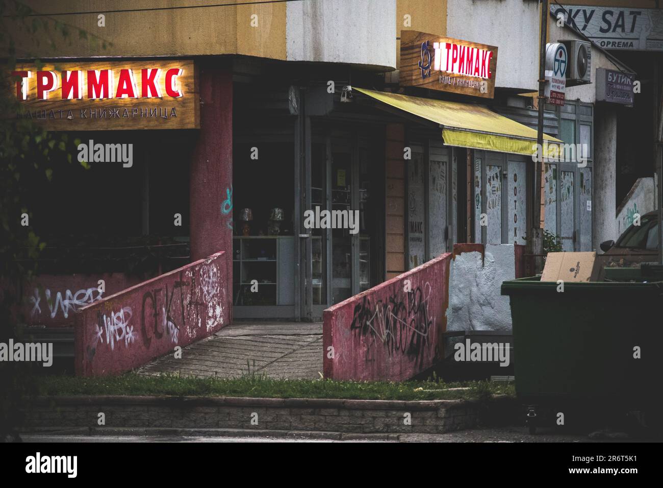 Laden Sie Trimaks mit Neon-Werbung und einem Müllcontainer vor sich in einer düsteren, gruseligen und beängstigenden Umgebung ein Stockfoto