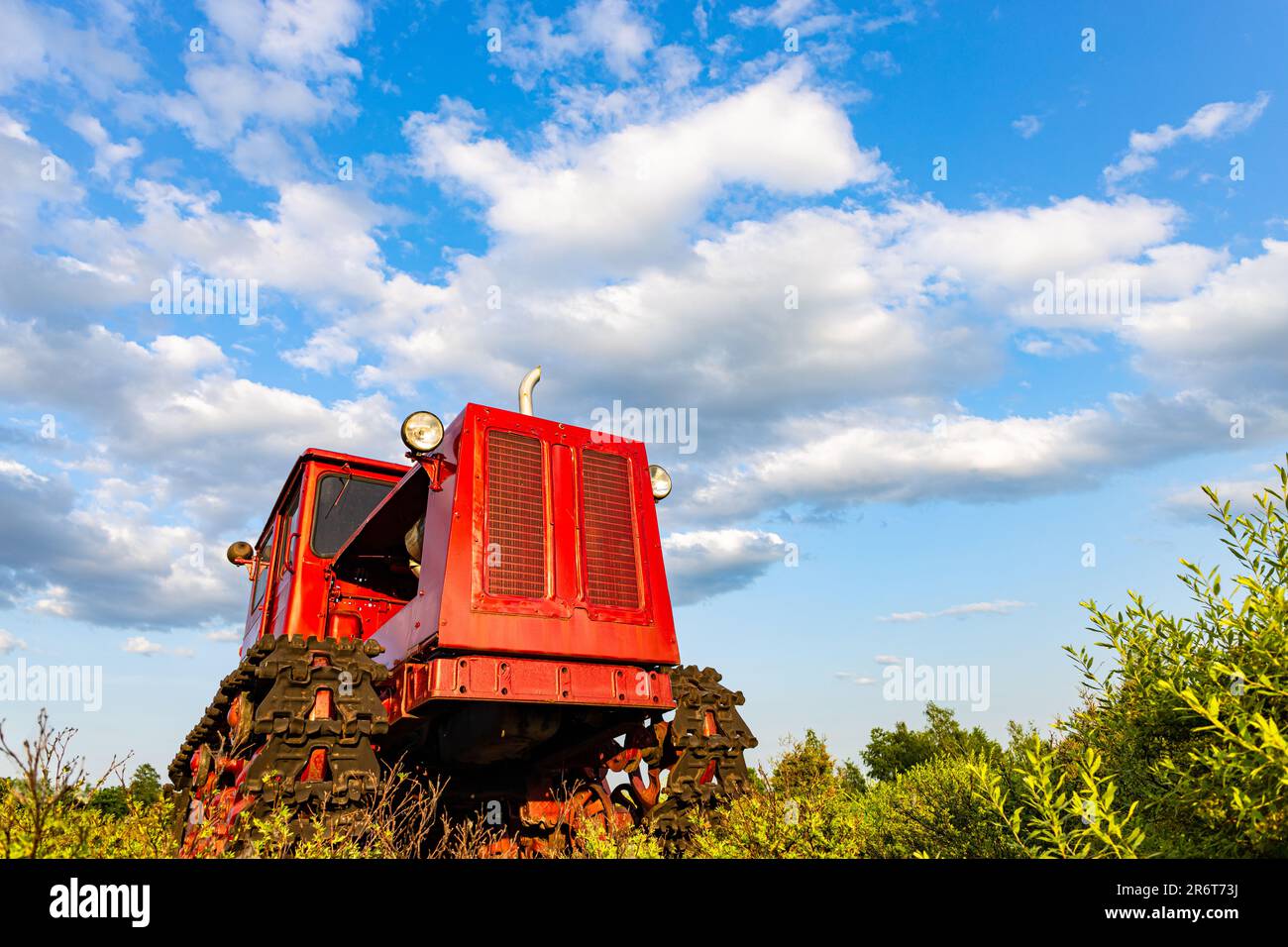 Der rote Traktor des alten Modells steht auf dem Feld. Roter alter Traktor. Traktor aus einem niedrigeren Winkel fotografiert. Der alte sowjetische Traktor steht auf dem Feld Stockfoto