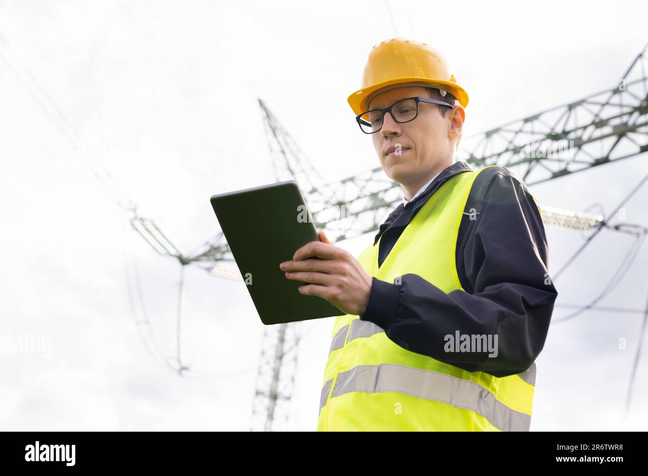 Ingenieur mit digitalem Tablet auf dem Hintergrund eines Stromleitungsturms. Stockfoto