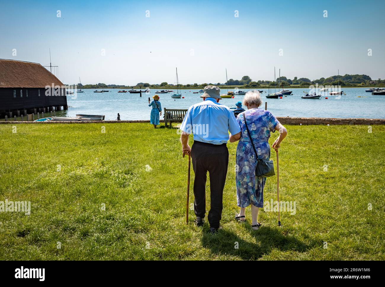 Ein älteres Ehepaar in den 90s Jahren ist durch eine grasbedeckte Gegend in Bosham neben Chichester Harbour, Großbritannien, gelaufen. Stockfoto