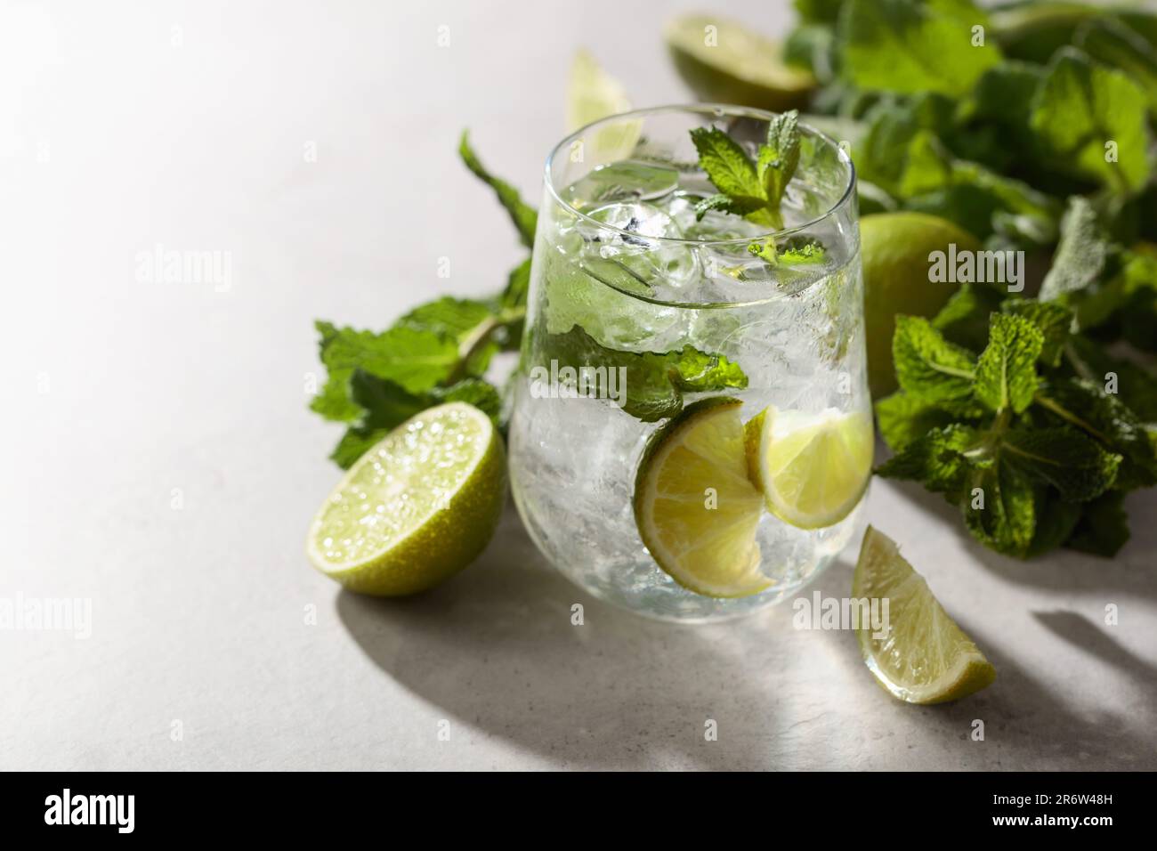 Mojito mit Eis, Limette und Minze auf einem weißen Steintisch. Kühles erfrischendes Getränk mit natürlichem Eis in einem beschlagenen Glas. Stockfoto