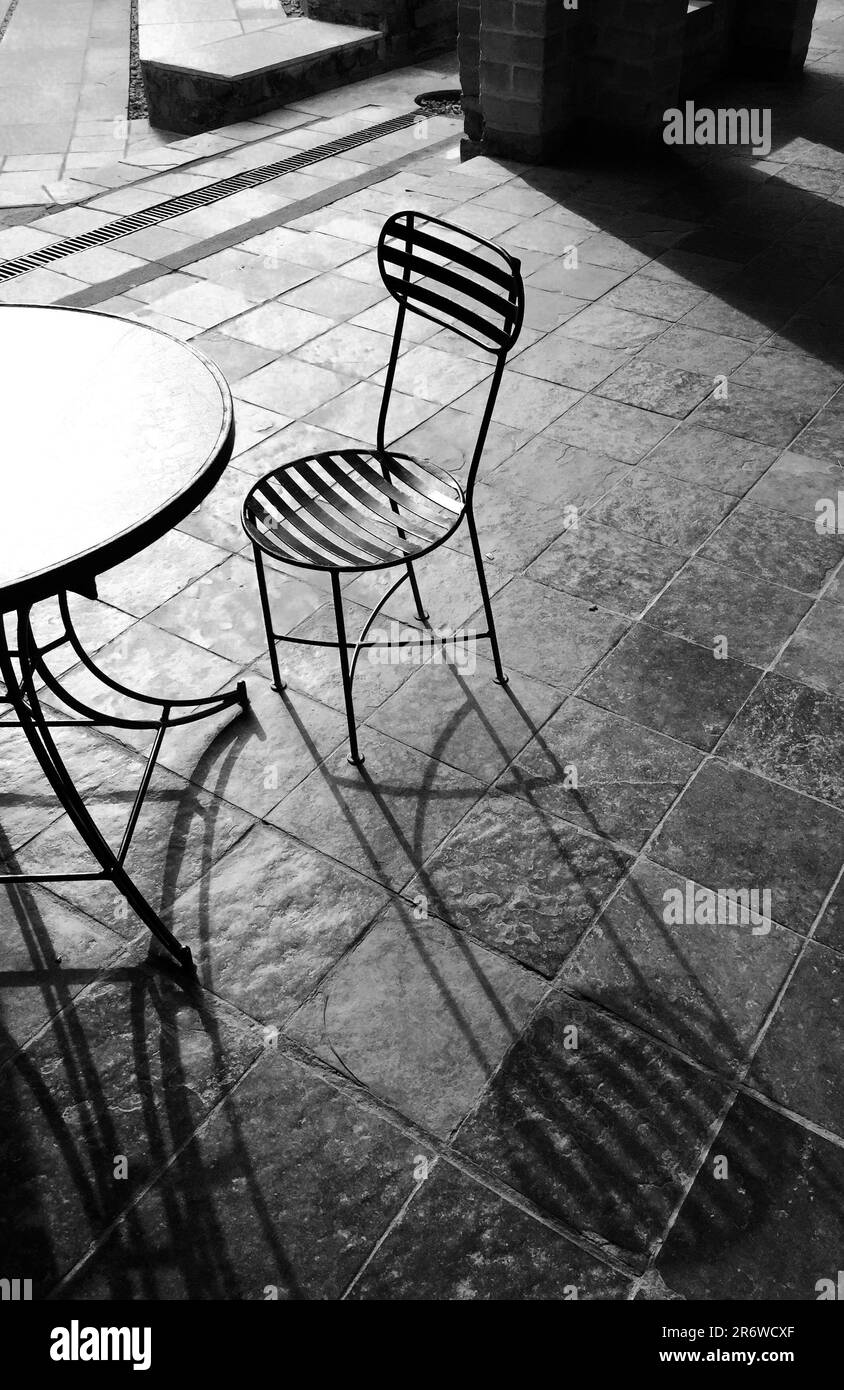 Ein schwarz-weißes Bild von zwei Stühlen an einem Tisch im Freien, der sich gegenüber befindet Stockfoto