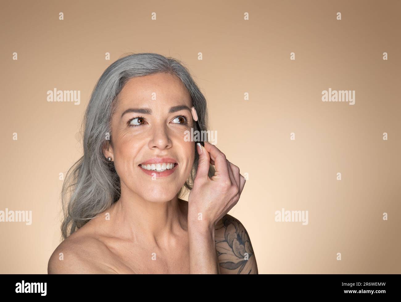 Glückliche grauhaarige ältere Frau, die die Augenbrauen mit Bürste putzt und lächelt, Schönheitsbehandlungen und Kosmetikprodukte genießt Stockfoto