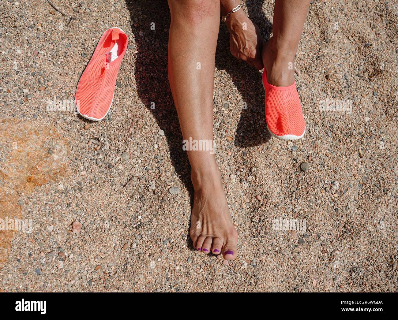 Zwei Beine mit einem orangefarbenen Strand Flip Flops im Sand im Sommerurlaub. Eine nicht wiedererkennbare Frau Stockfoto