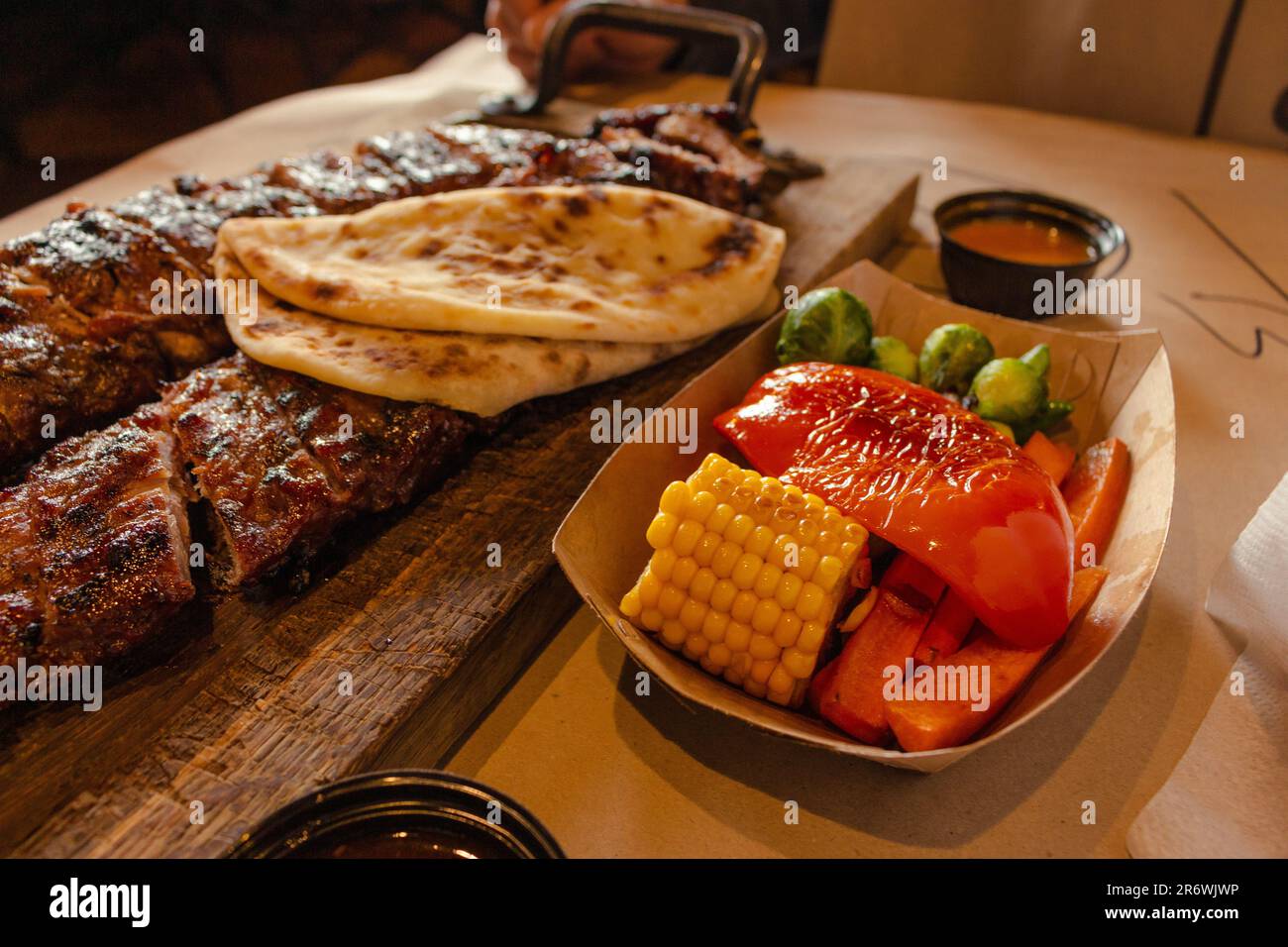 Gegrillte Rippchen mit Gemüse und Brot. Geräuchertes Schweinefleisch auf Holzbrett und gegrilltes Gemüse. Abendmenü im Restaurant. Mittellang geröstetes Steak mit Mais. Stockfoto