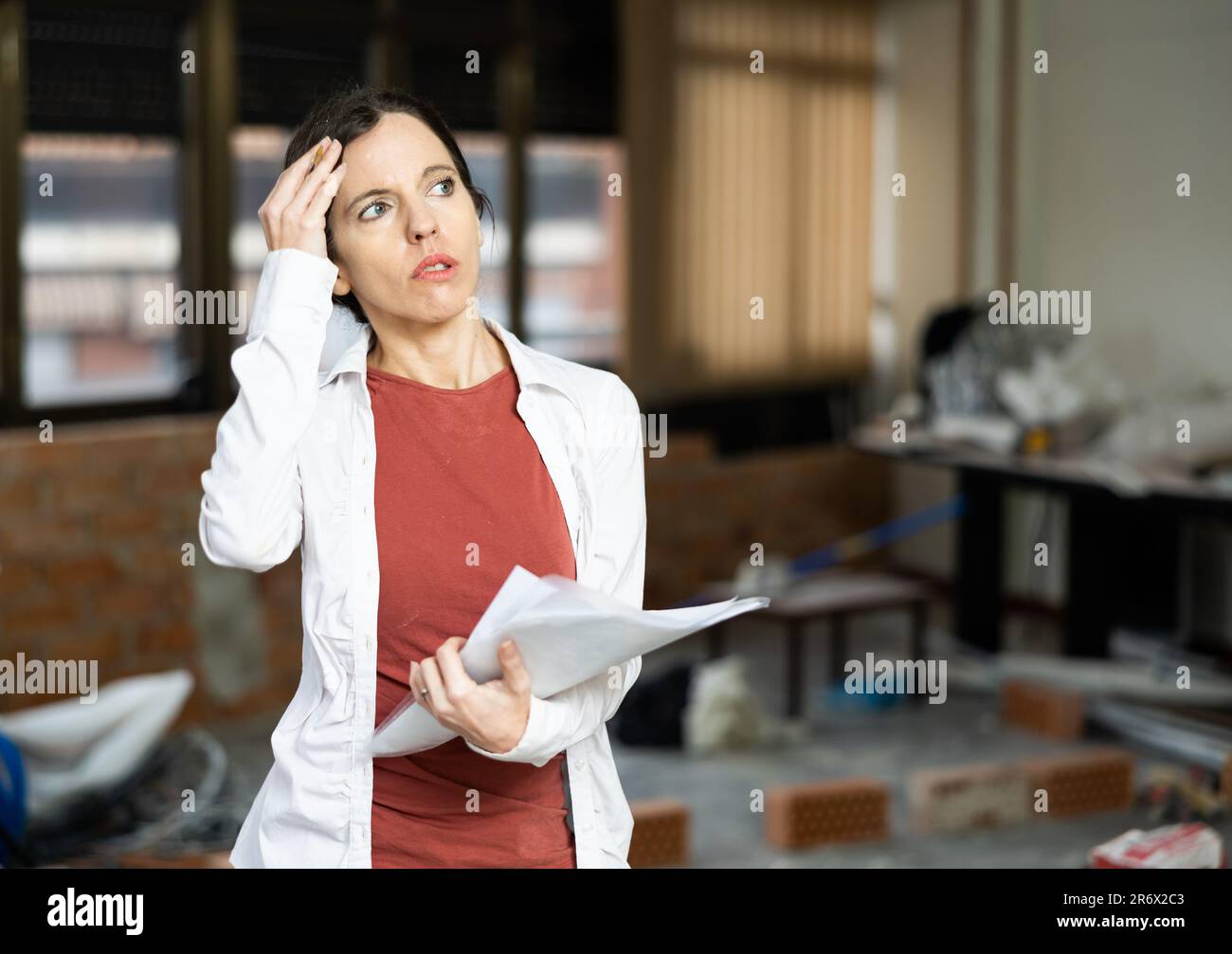 Rätselhafte Frau, die das Haus während der Renovierung untersucht und mit Blaupausen vergleicht Stockfoto