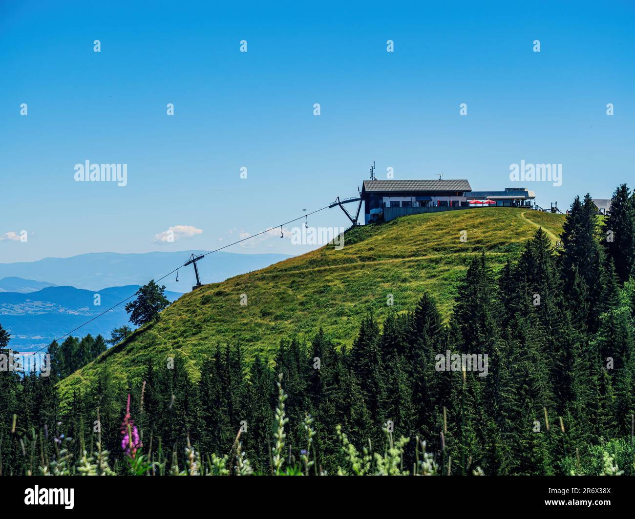 Panoramablick vom Dreilandereck Österreich, Slowenien, Italien, Kärnten, mit Skilift, Sessellift, Straßenbahngebäuden, Gebirgsdach mit klarem Himmel, Kiefernwald Stockfoto