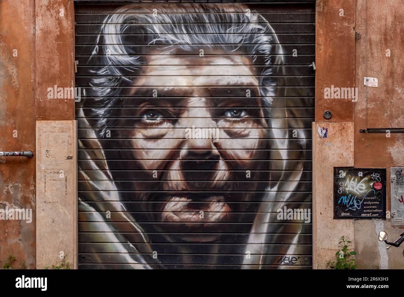 Ein Porträt des Gesichts einer alten Frau, gemalt auf einer Metalltür mit Rollläden in der Gegend von Trastevere in Rom, Italien Stockfoto
