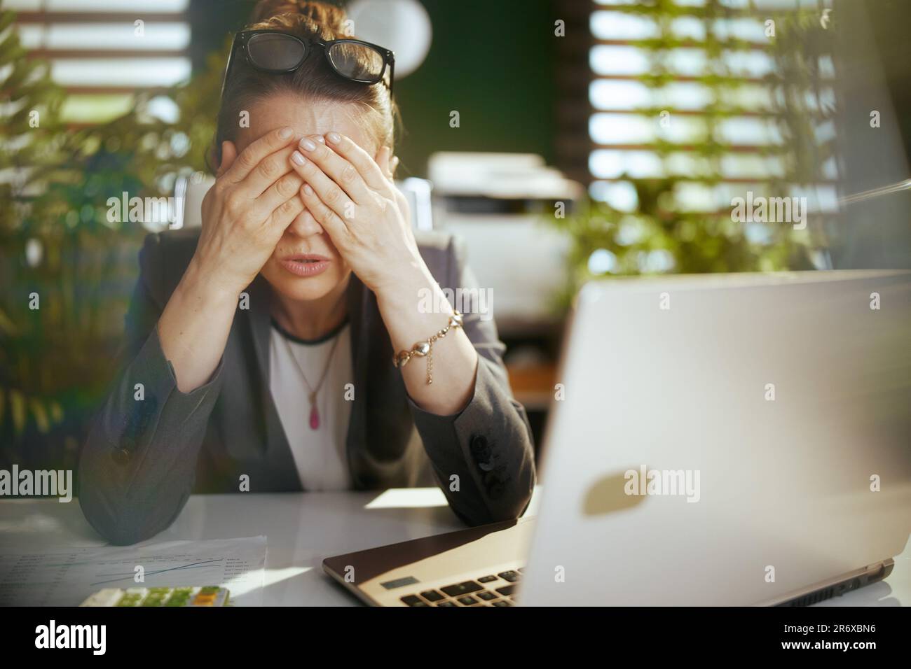 Nachhaltiger Arbeitsplatz. Moderne Geschäftsfrau bei der Arbeit mit einem Laptop, die Augenübungen macht. Stockfoto