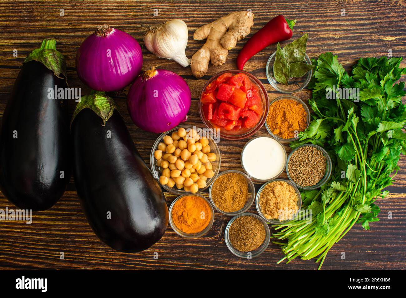 Vegan geröstete Auberginen- und Kichererbsen-Curry-Zutaten: Rohe Auberginen, rote Zwiebeln, Gewürze und andere indische Curryzutaten Stockfoto