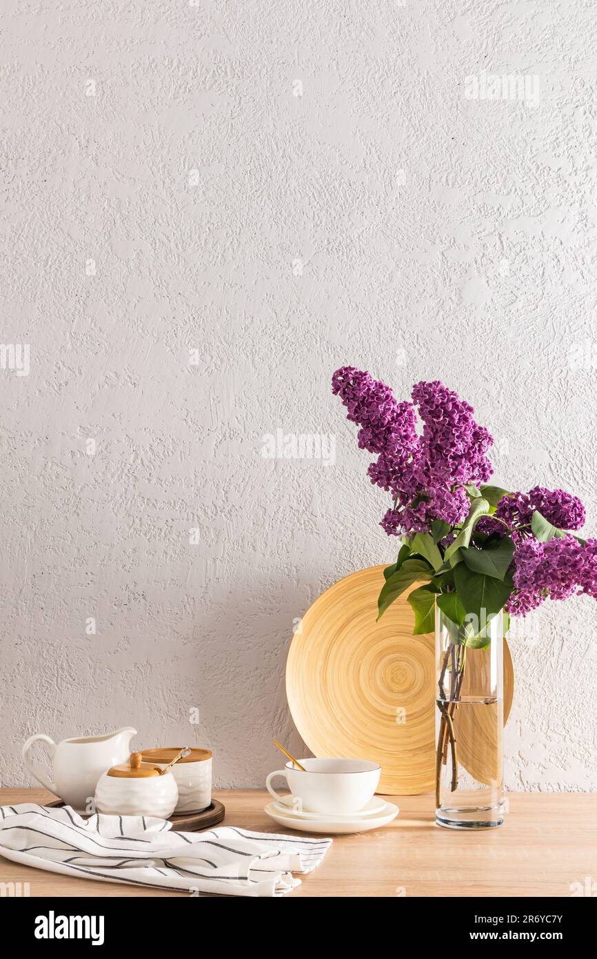 Tee-Utensilien und eine Tasse Tee auf der Küchenablage aus Holz. Eine graue Zementwand und eine Vase aus Flieder. Vertikale Ansicht. Ein Kopierbereich Stockfoto