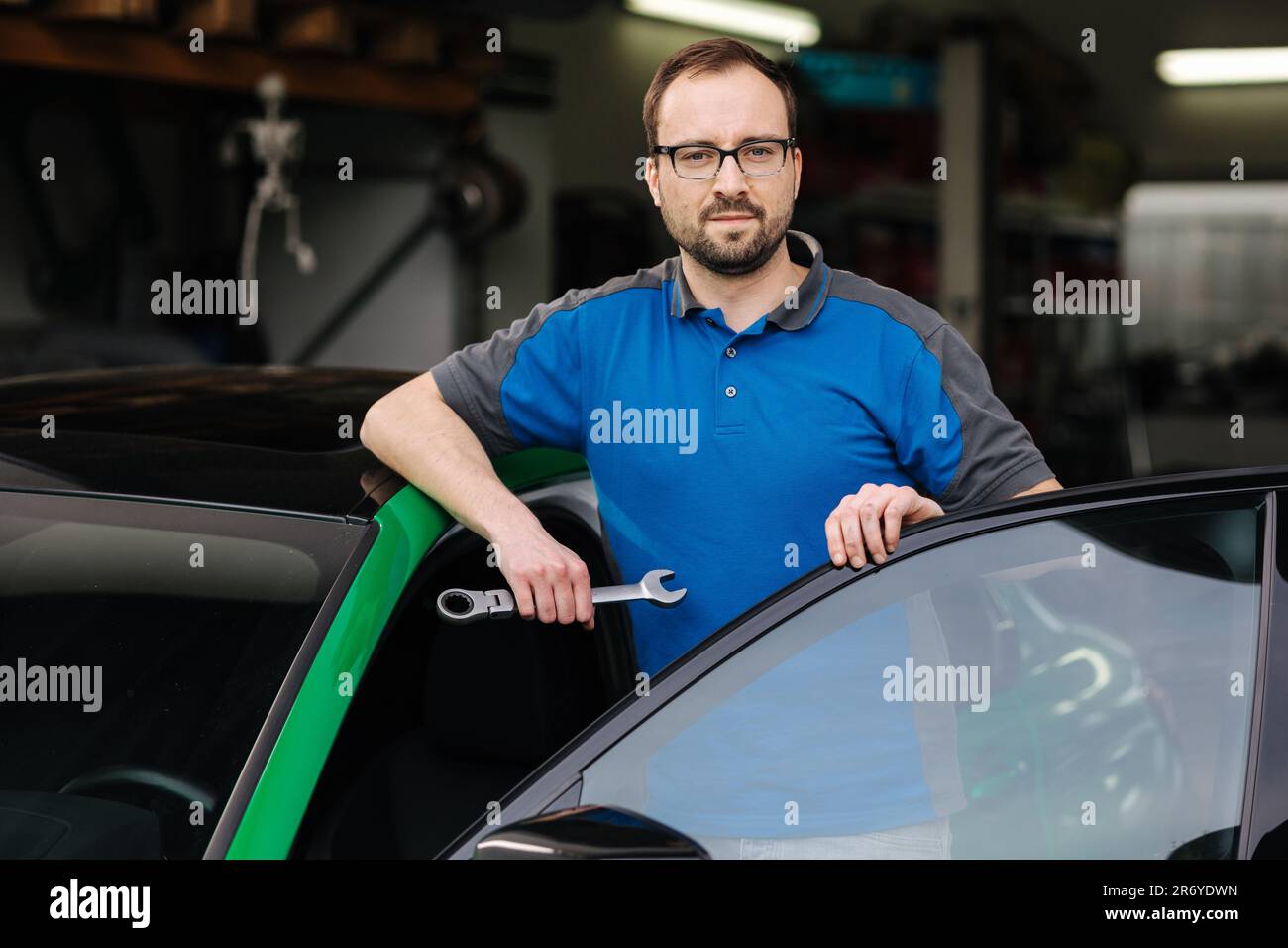 Ein gutaussehender Mechaniker hält das Auto-Reparaturwerkzeug und lehnt sich mit seinem Ellbogen auf das Dach Stockfoto