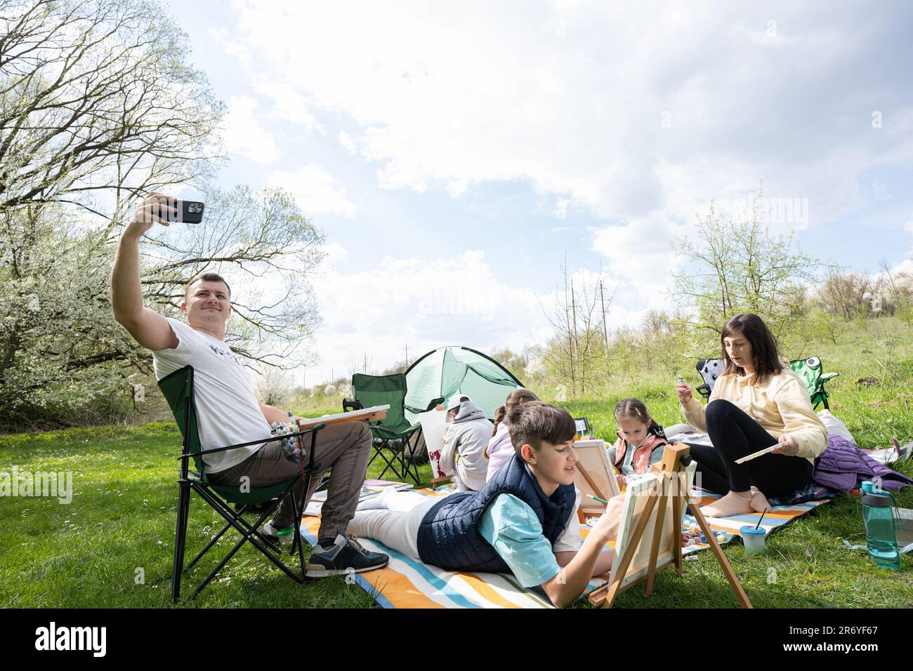 Dad leitet einen Vlog. Glückliche junge Familie, die Spaß hat und draußen auf einer Picknickdecke im Garten Spring Park, Entspannung. Stockfoto