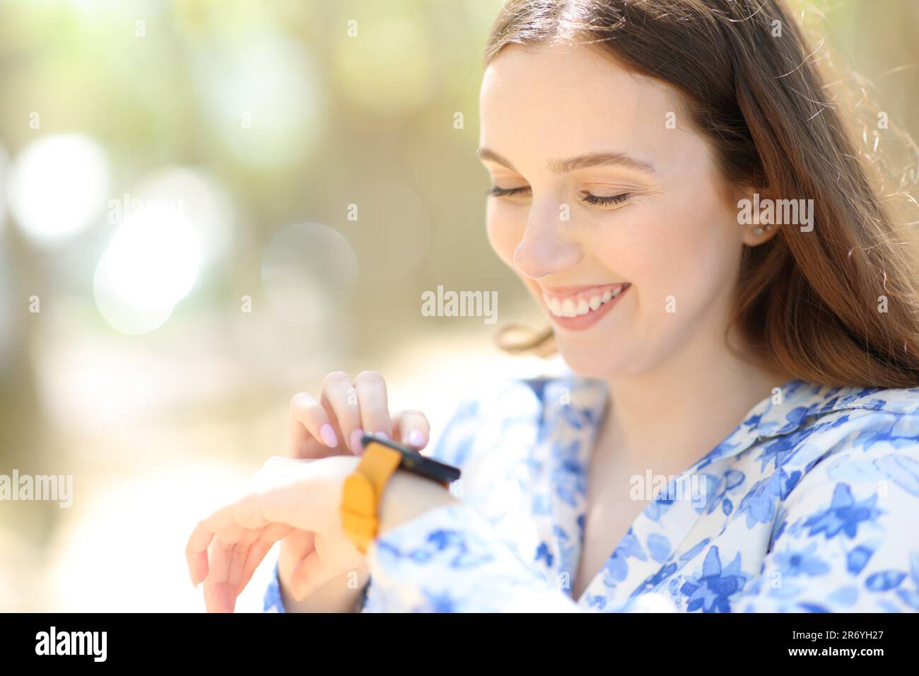 Glückliche Frau, die in einem sonnigen Park mit Smartwatch steht Stockfoto