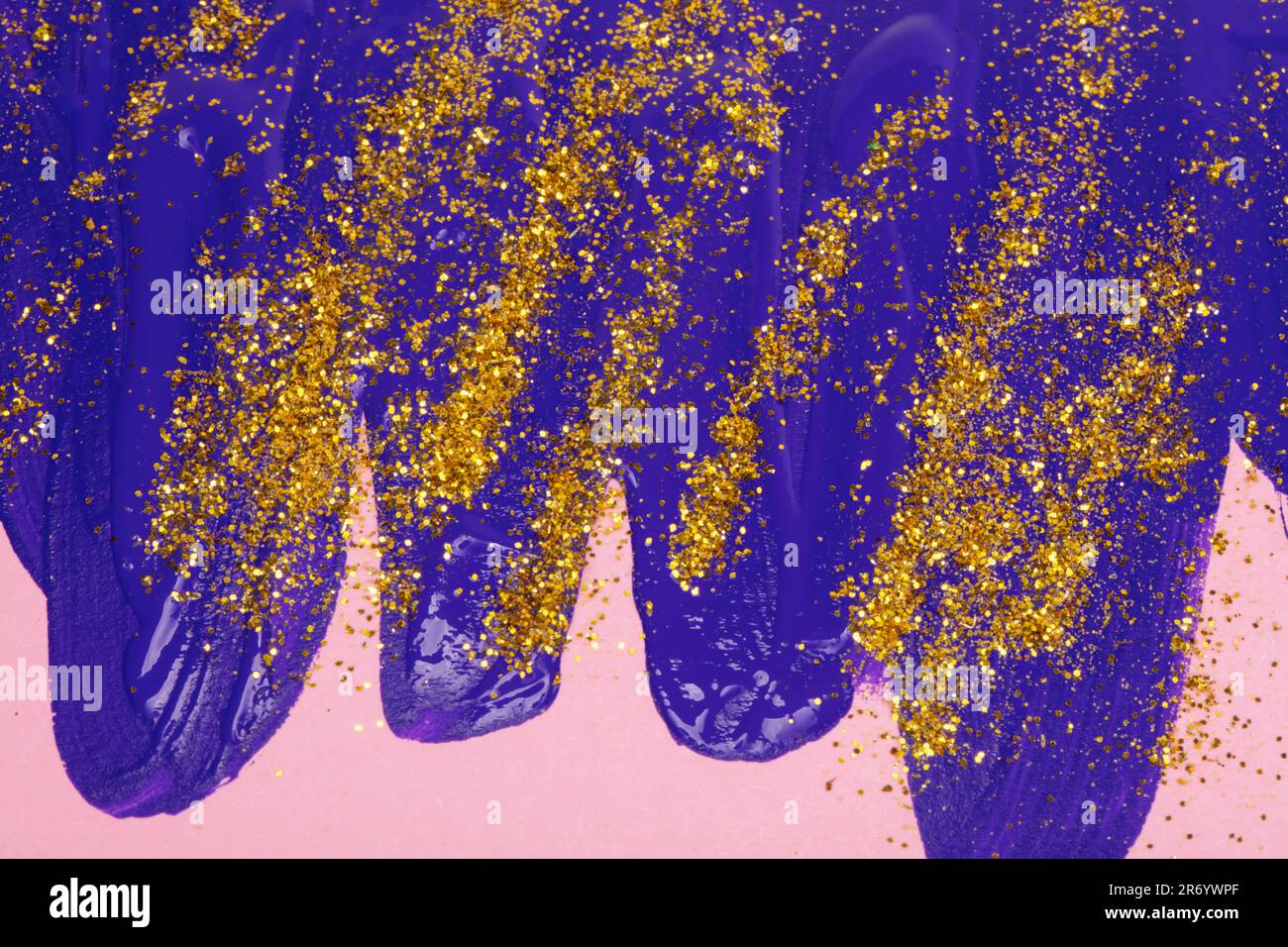 Auf rosafarbenem Hintergrund, blaue schillernde Flecken von fließender Acrylfarbe mit goldenen Glitzern. Stockfoto