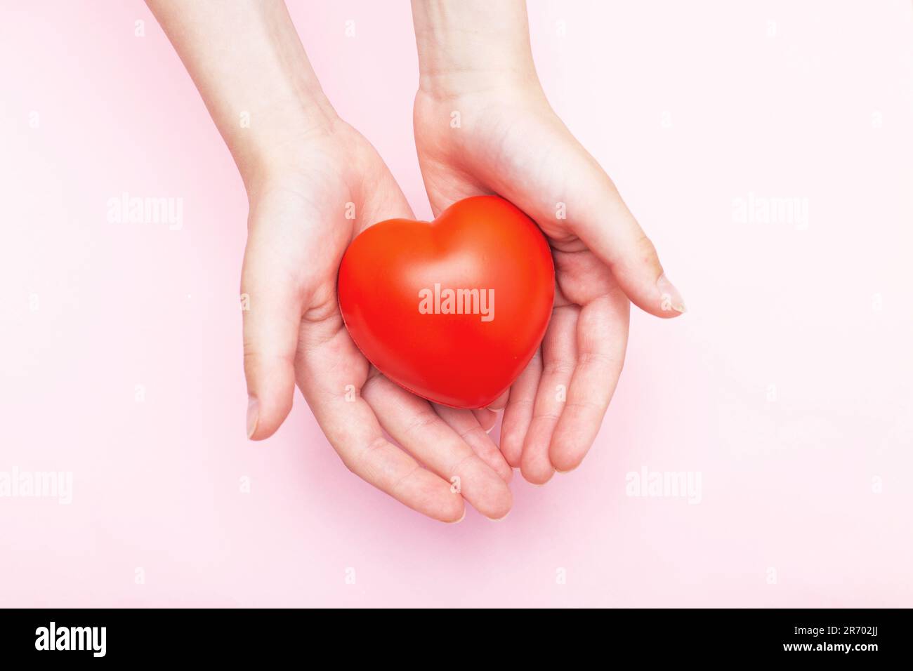 Kinderhände halten ein rotes Herz als Symbol für Pflege, Liebe, Unterstützung und Schutz isoliert auf pinkfarbenem Hintergrund. Kindergesundheitskonzept. Stockfoto