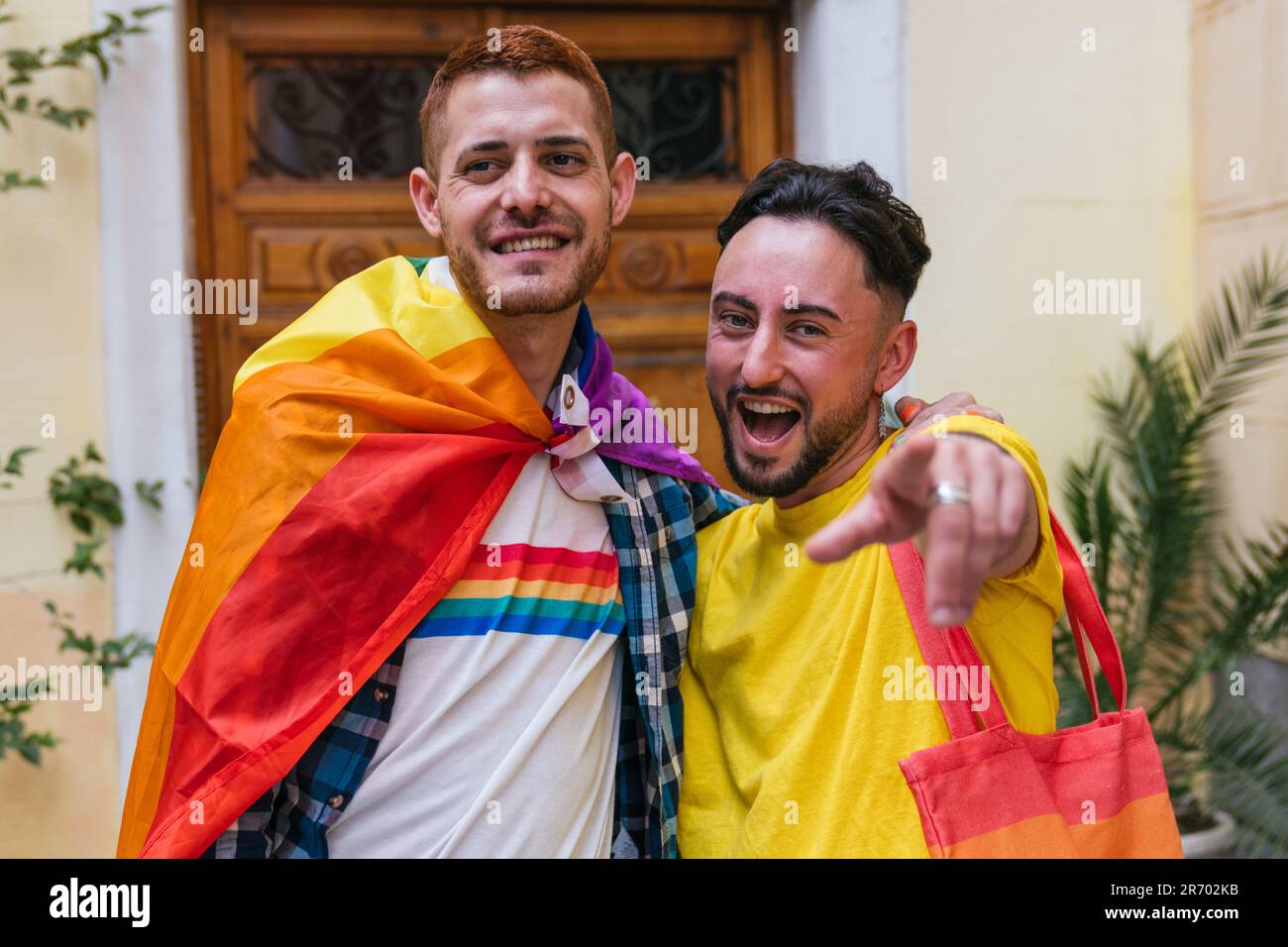 Fröhliche schwule Freunde: Stolz annehmen, auf die Kamera zeigen, mit LGBT-Symbolen geschmückt, nach Hause gehen Stockfoto