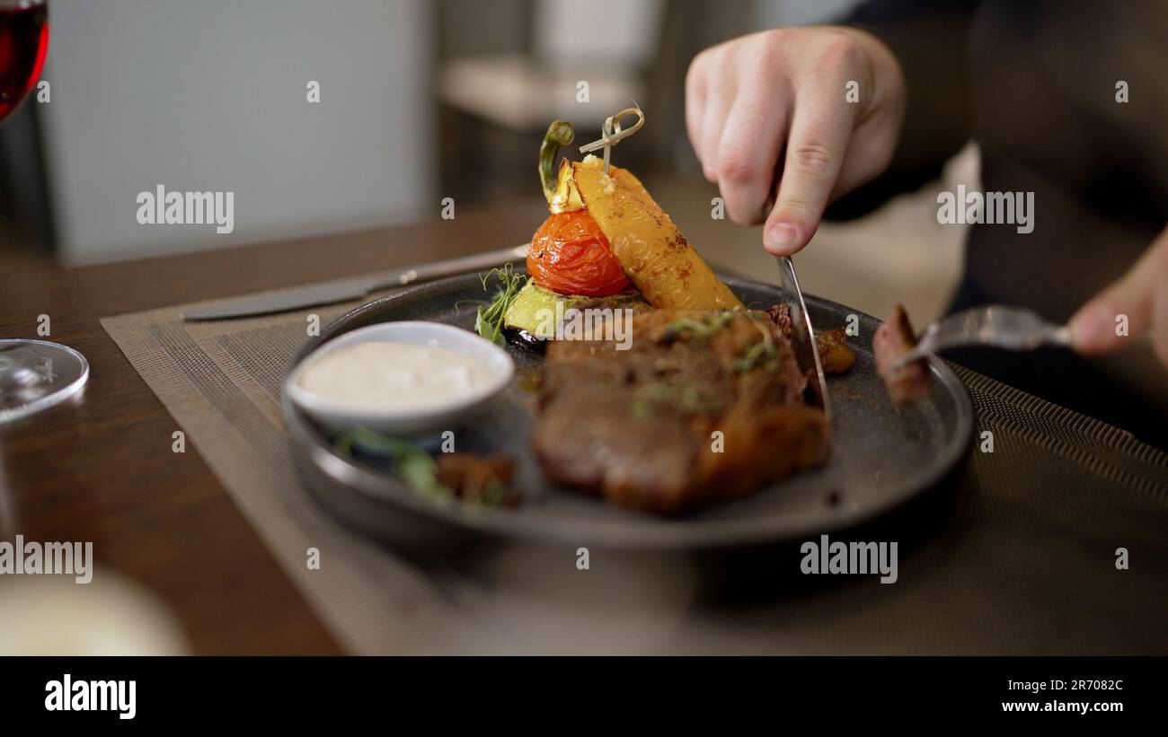 Ein Mann schneidet ein gekochtes Steak aus mittelgroßen Rippchen. Köstliches Steak mit Gemüse auf dem Tisch. Ein Mann in einem Restaurant isst, schneidet Fleisch mit einem Messer. Stockfoto