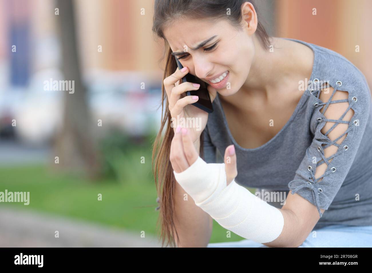 Genesungsfrau mit Bandarm ruft Arzt am Telefon und sitzt auf der Straße Stockfoto
