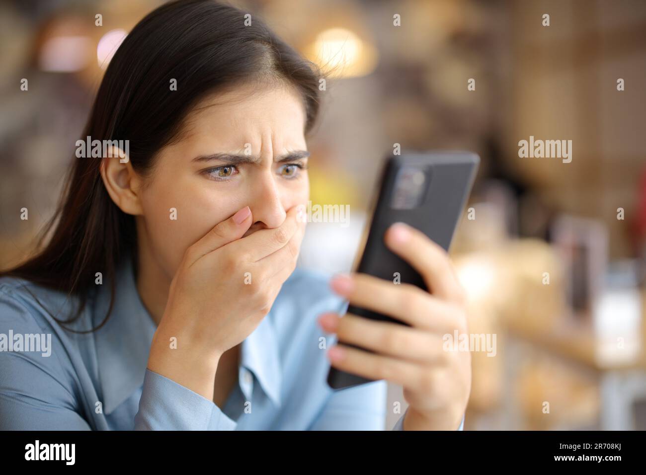 Verängstigte Frau, die sich Medieninhalte am Telefon in einem Restaurant ansieht Stockfoto