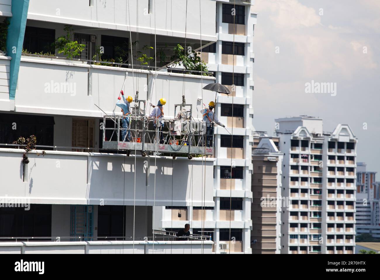 Arbeiter, die einen Industrieleiter benutzen, der in der Luft hängt und unter der heißen Sonne einen Gebäudeaußenbereich lackiert. Ein sehr risikoreicher Beruf. Stockfoto