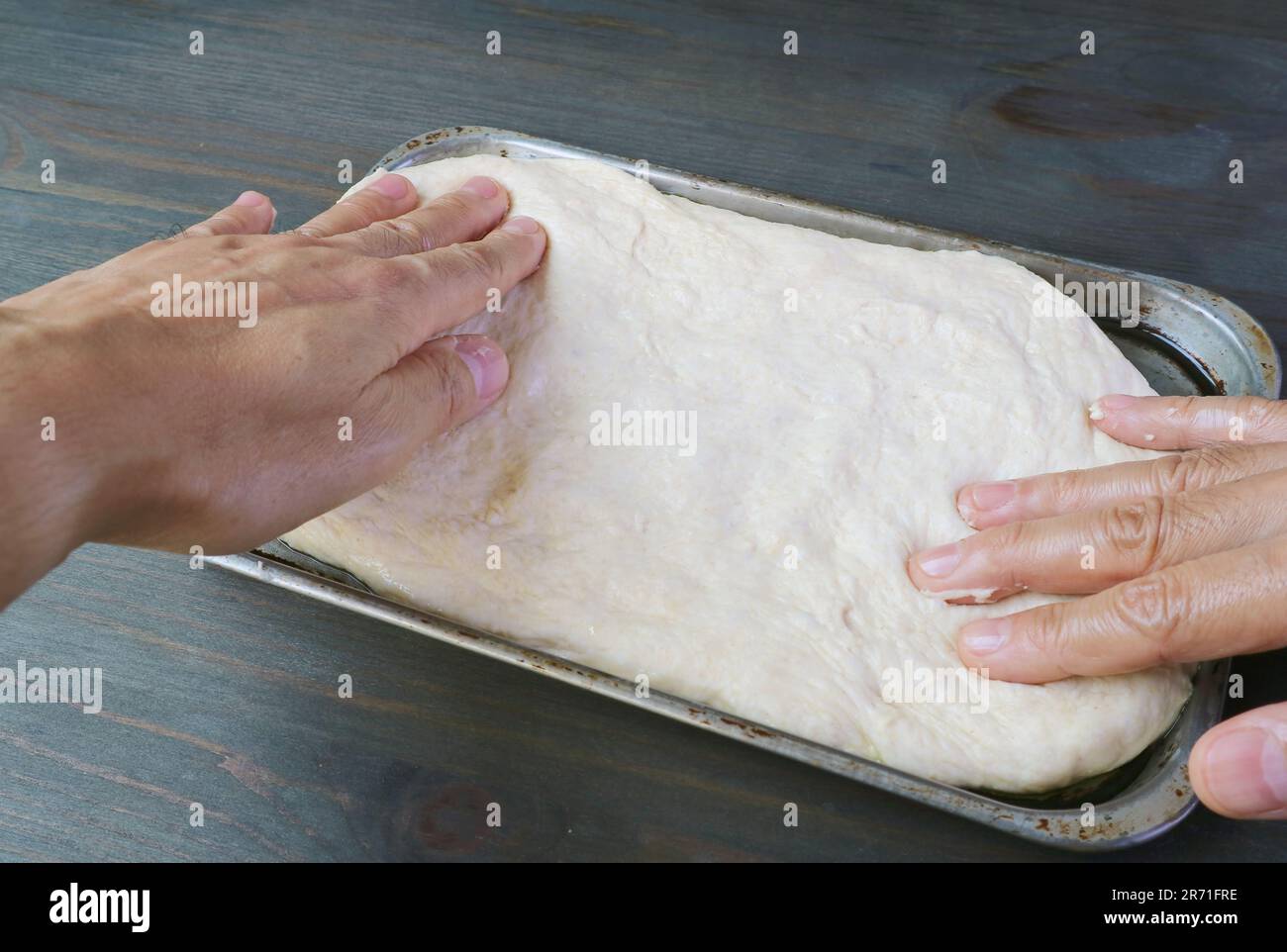 Die Hände strecken den Teig in einem Topf, um Pizza zu backen Stockfoto