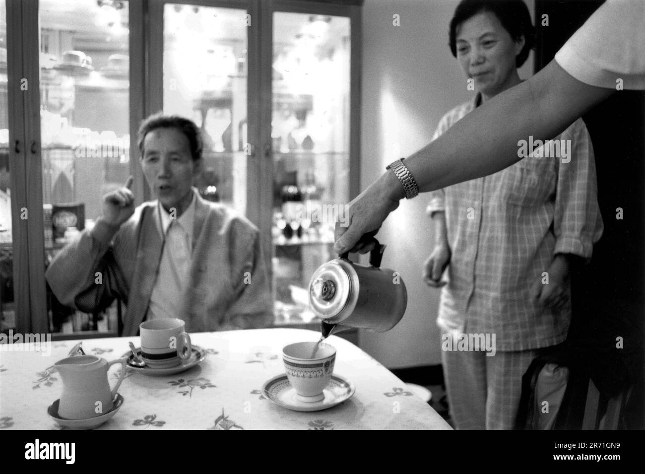 Shanghai China 2000. Der gefeierte Shanghai-Miniaturbildhauer Zhou Changxing trinkt bei einem Freund Kaffee. Es gilt als sehr westlich für Menschen seiner Generation, Kaffee zu trinken, aber seit dem Auftauchen von Starbucks Coffee in Shanghai im Jahr 1999 hat das Getränk begonnen, junge Leute anzuziehen, da der Coffee Shop ein guter Ort ist, um Freunde zu treffen. Lockere und bequeme Kleidung in Form eines Schlafanzugs wird in Shanghai wie in den 1920er Jahren häufig in Innenräumen getragen, und das Tragen von P.j.s außerhalb der Türen ist nicht ungewöhnlich, vor allem im Sommer. 2000s HOMER SYKES Stockfoto