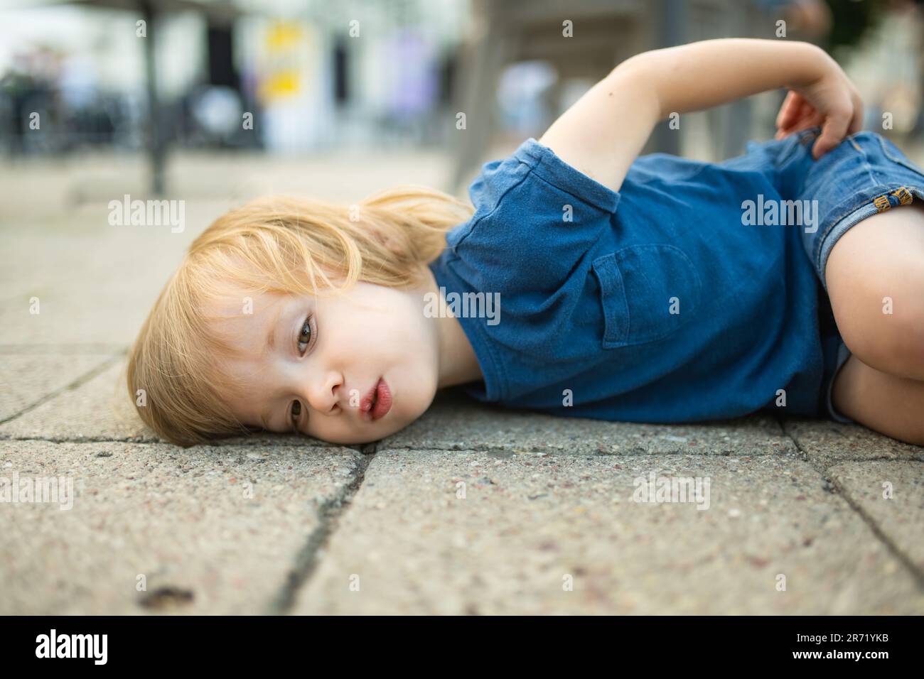 Ein kleiner Junge, der draußen auf dem Boden liegt. Unartiges Kind auf der Straße. Stockfoto