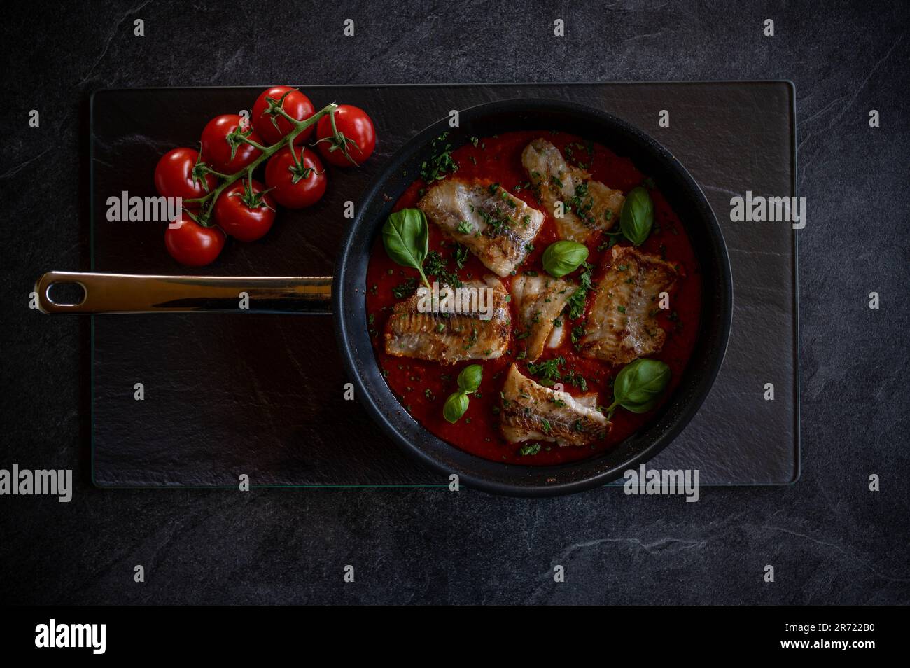 Gebratener Fisch in einer scharfen Tomatensoße auf dunklem Hintergrund. Schwache Beleuchtung Stockfoto