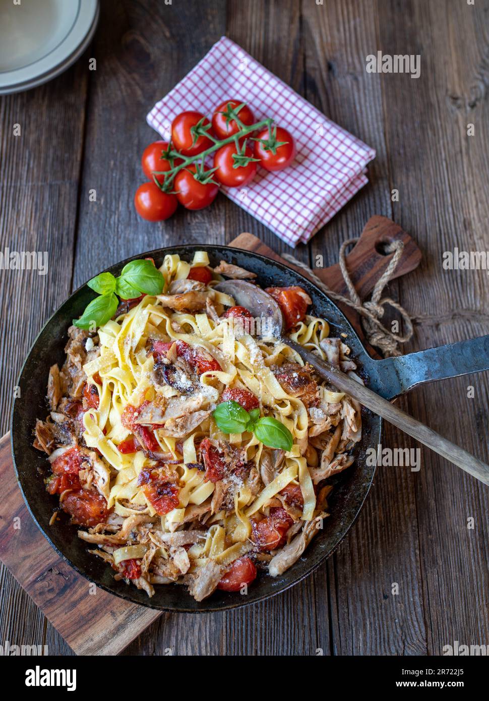 Pasta mit geröstetem Hühnerfleisch, Tomaten, Zwiebeln, Knoblauch und Kräutern in einer Pfanne auf einem Holztisch Stockfoto