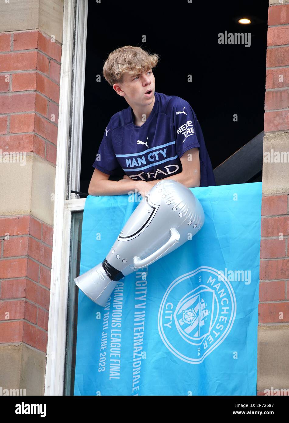 Ein Fan, der vor der Treble Parade in Manchester eine aufblasbare Trophäe in einem Fenster hält. Manchester City schloss die Treble (Champions League, Premier League und FA Cup) nach einem Sieg von 1-0 über Inter Mailand in Istanbul und sicherte ihnen den Ruhm der Champions League. Foto: Montag, 12. Juni 2023. Stockfoto