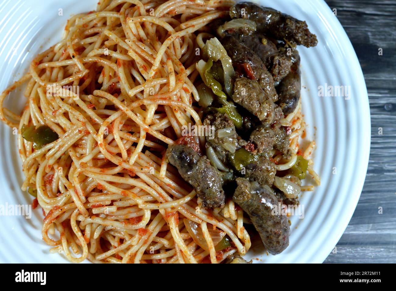 Ein Teller mit gekochtem Rindfleisch aus dem Nahen Osten, ägyptischen Würsten mit grünem Paprika, Zwiebeln, Knoblauch, Tomaten, schwarzem Pfeffer und Öl sowie klassischen Spaghetti Stockfoto