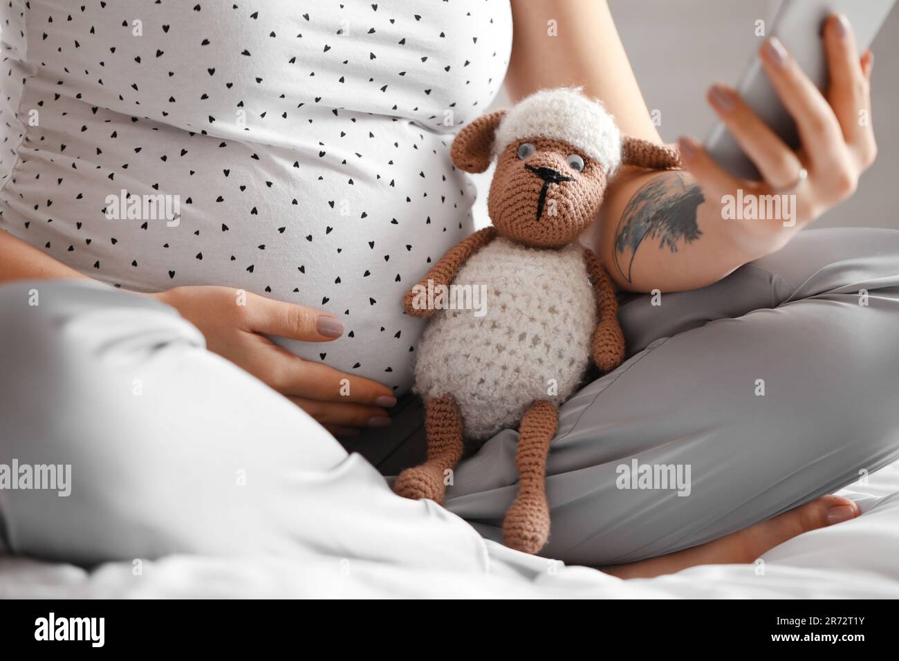 Junge schwangere Frau mit Spielzeug, die ein Handy im Schlafzimmer benutzt, Nahaufnahme Stockfoto