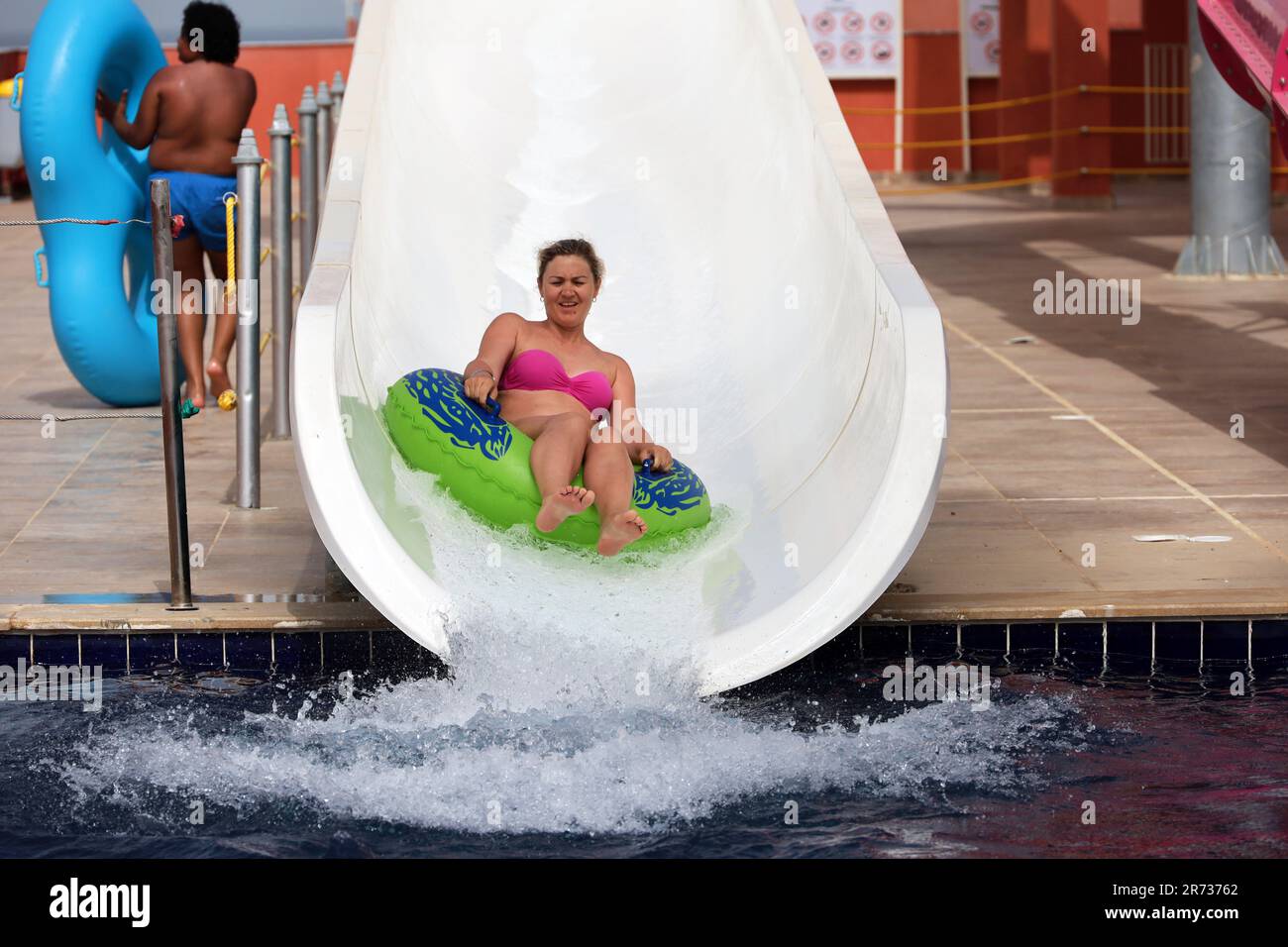 Glückliche Frau im aufblasbaren Kreis fährt auf der Wasserrutsche im Aqua Park. Fahrt auf der Wasserröhre, Sommerurlaub genießen, Strandresort Stockfoto