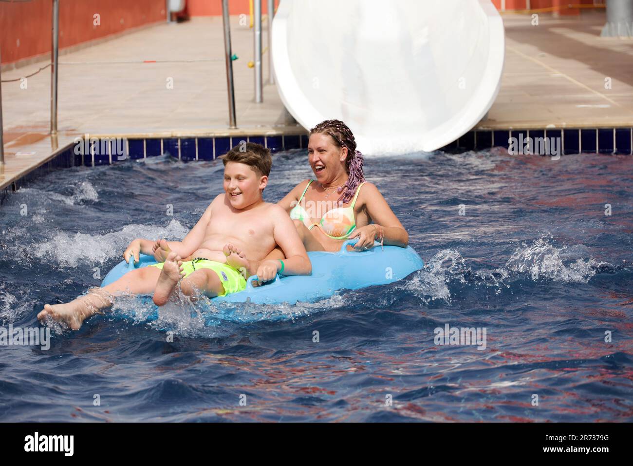 Glückliche Frau und Junge im aufblasbaren Kreis rollten auf der Wasserrutsche im Aqua Park herunter. Auf dem Wasserrohr fahren, Spaß haben Stockfoto