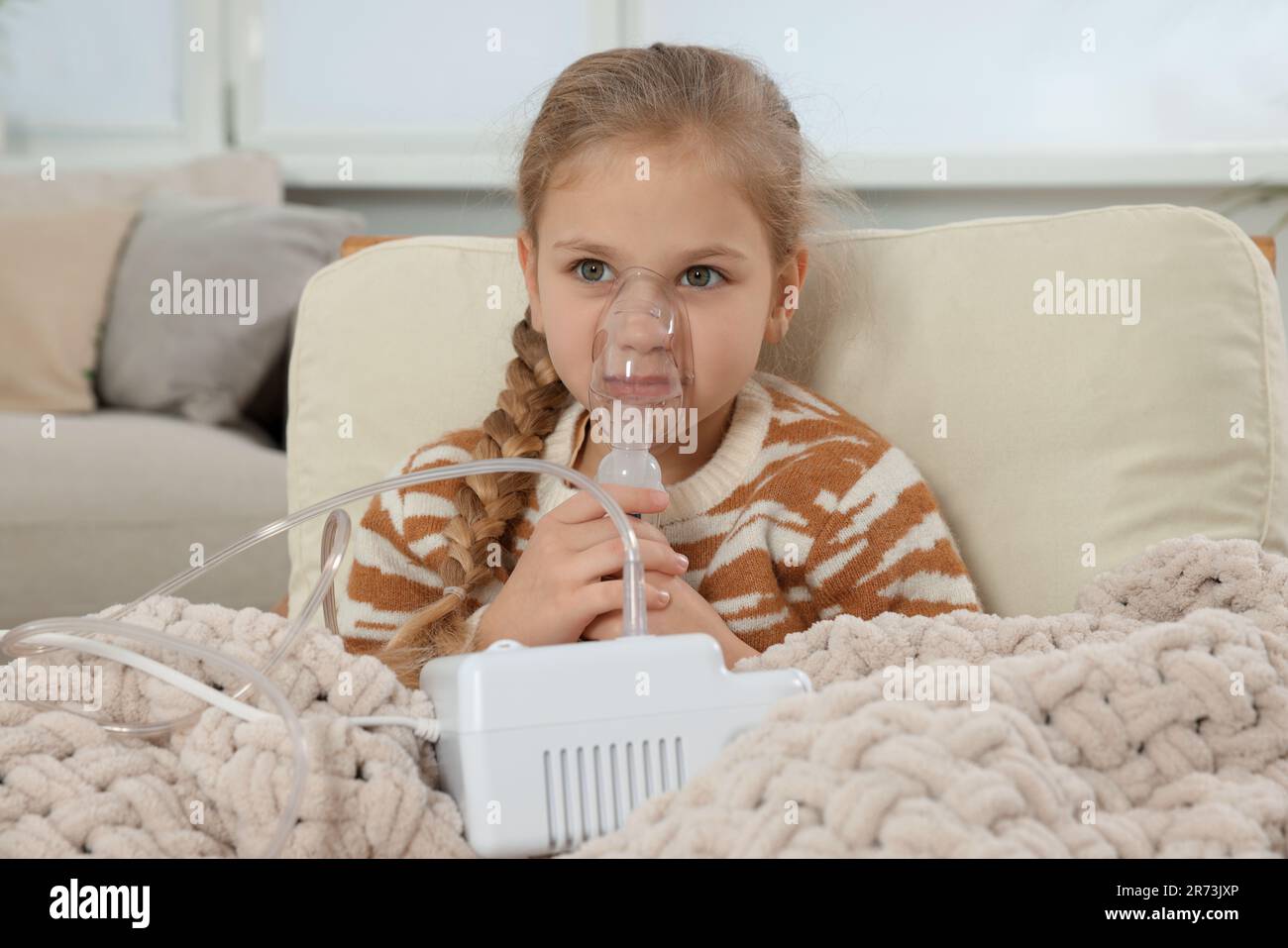 Kleines Mädchen mit Vernebler zur Inhalation im Sessel zu Hause Stockfoto