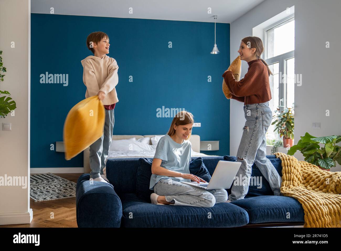 Mutter, die an einem Laptop arbeitet, während ihre aktiven, lauten Kinder mit Kissen spielen und Spaß haben Stockfoto