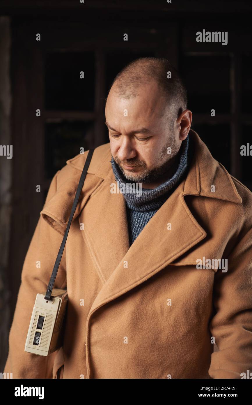 Ein Mann in einem großen Mantel mit einem Retro-Radio schaut nach unten. Stockfoto