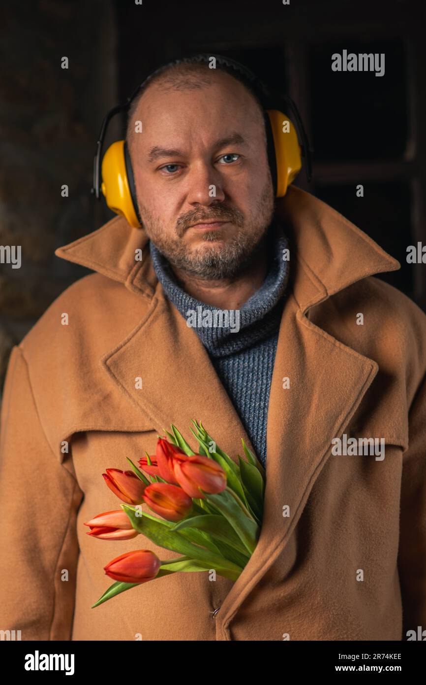 Lustiges Foto eines Mannes mit Kopfhörern aus Lärm mit einem Strauß Tulpen im Mantel. Stockfoto