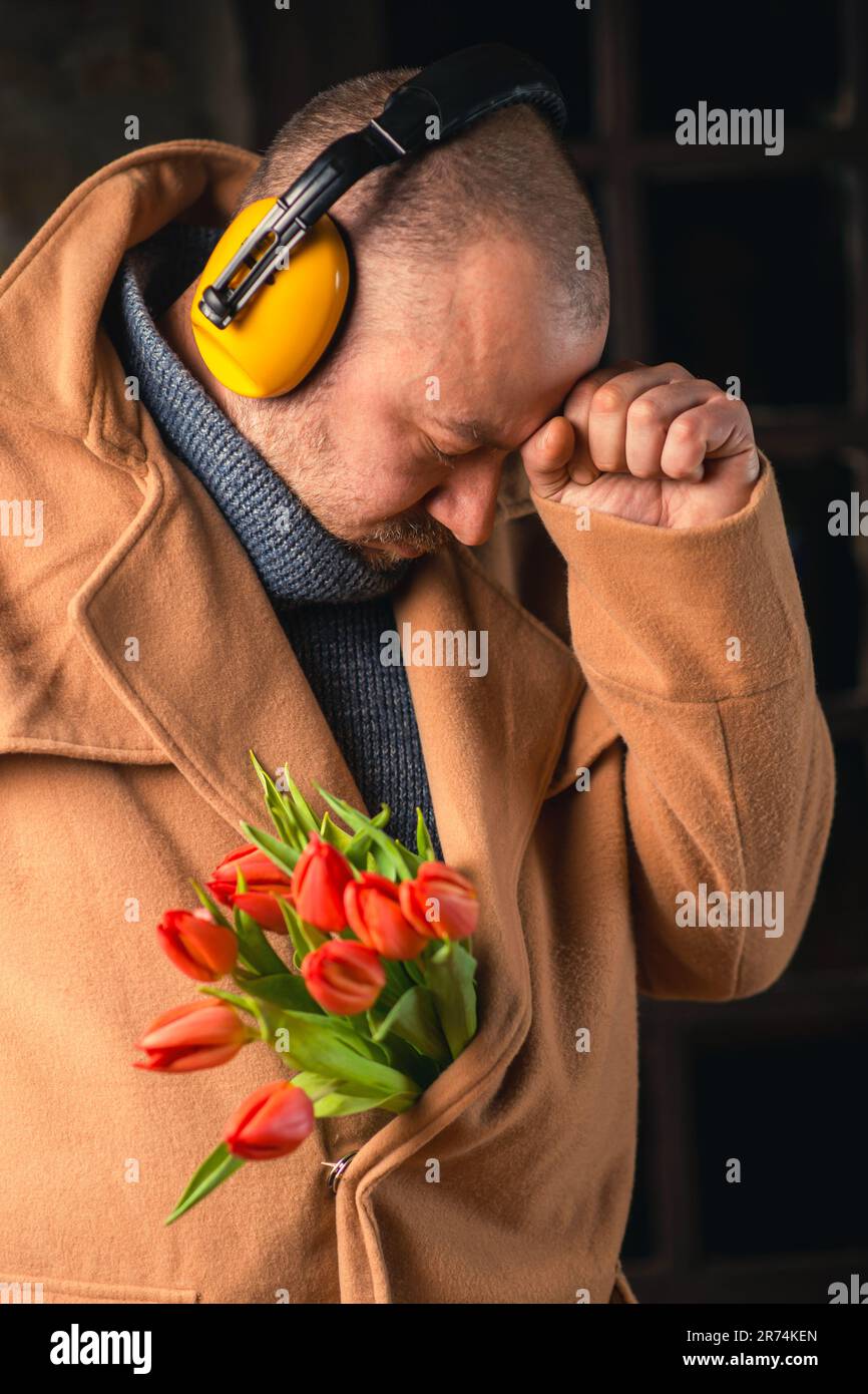 Lustiges Foto eines traurigen Mannes mit Kopfhörern und einem Strauß Tulpen im Mantel. Stockfoto