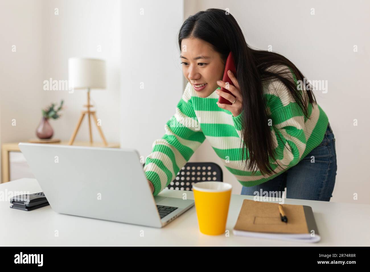 Junge asiatische Geschäftsfrau, die ein Notebook benutzt und mit einem Kollegen telefonisch im Büro spricht Stockfoto