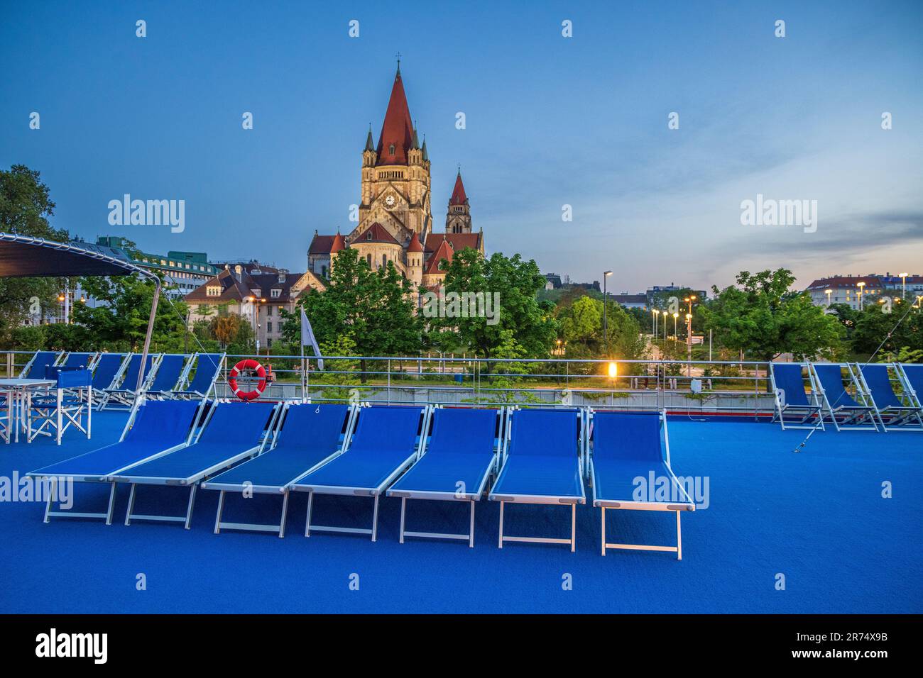Sonnenliegen auf dem Oberdeck mit der Kirche St. Franziskus von Assisi an der Donau, Wien, Österreich Stockfoto
