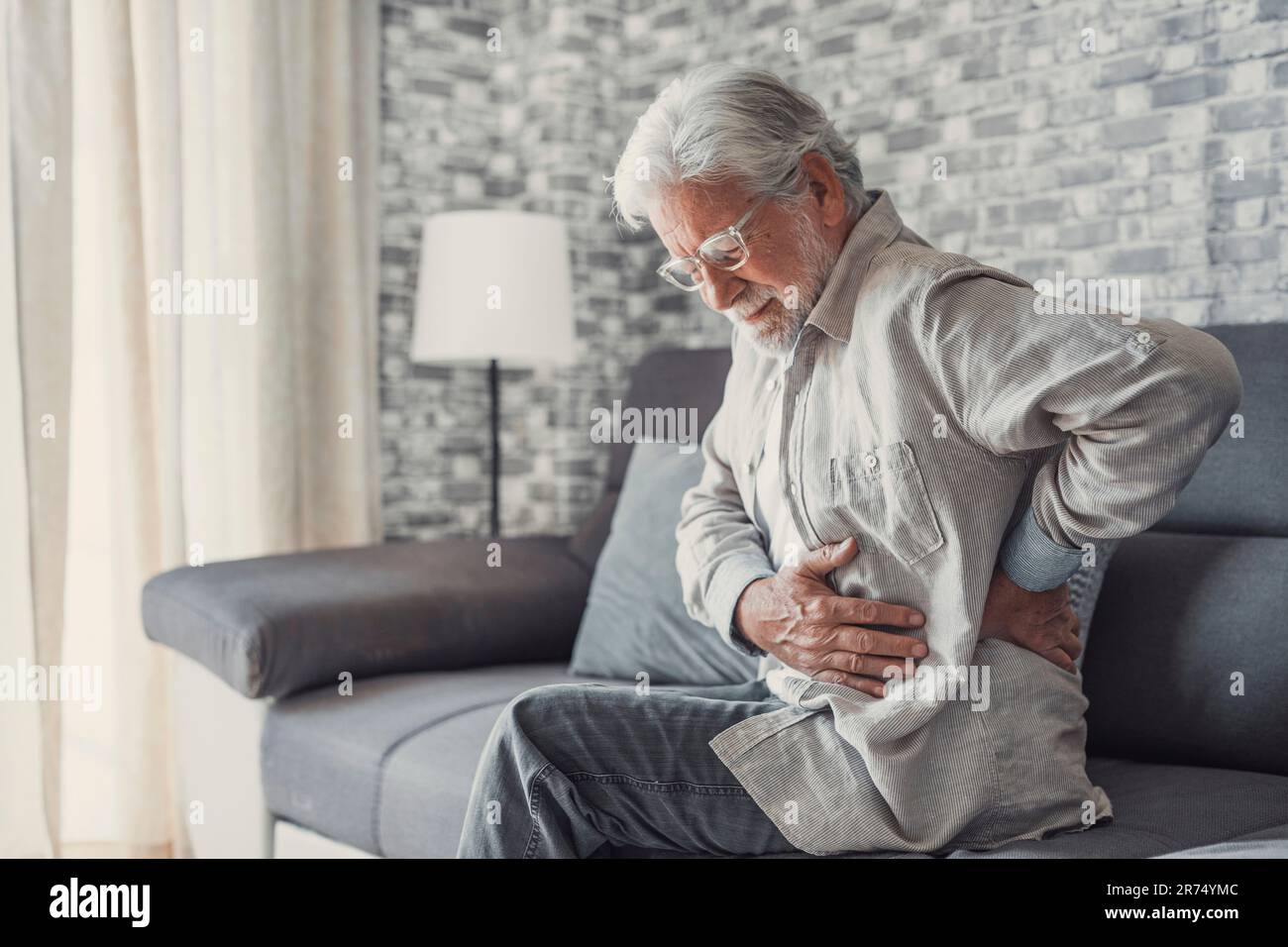 Aufgebrachter älterer Mann fühlt plötzliche Rückenschmerzen Muskelschmerzen Spannungsverletzung zu Hause sitzend, trauriger alter Großvater berührt Wirbelsäule mit Rückenschmerzen im unteren Lumbago Arthrose, Rückenschmerzen Konzept Stockfoto